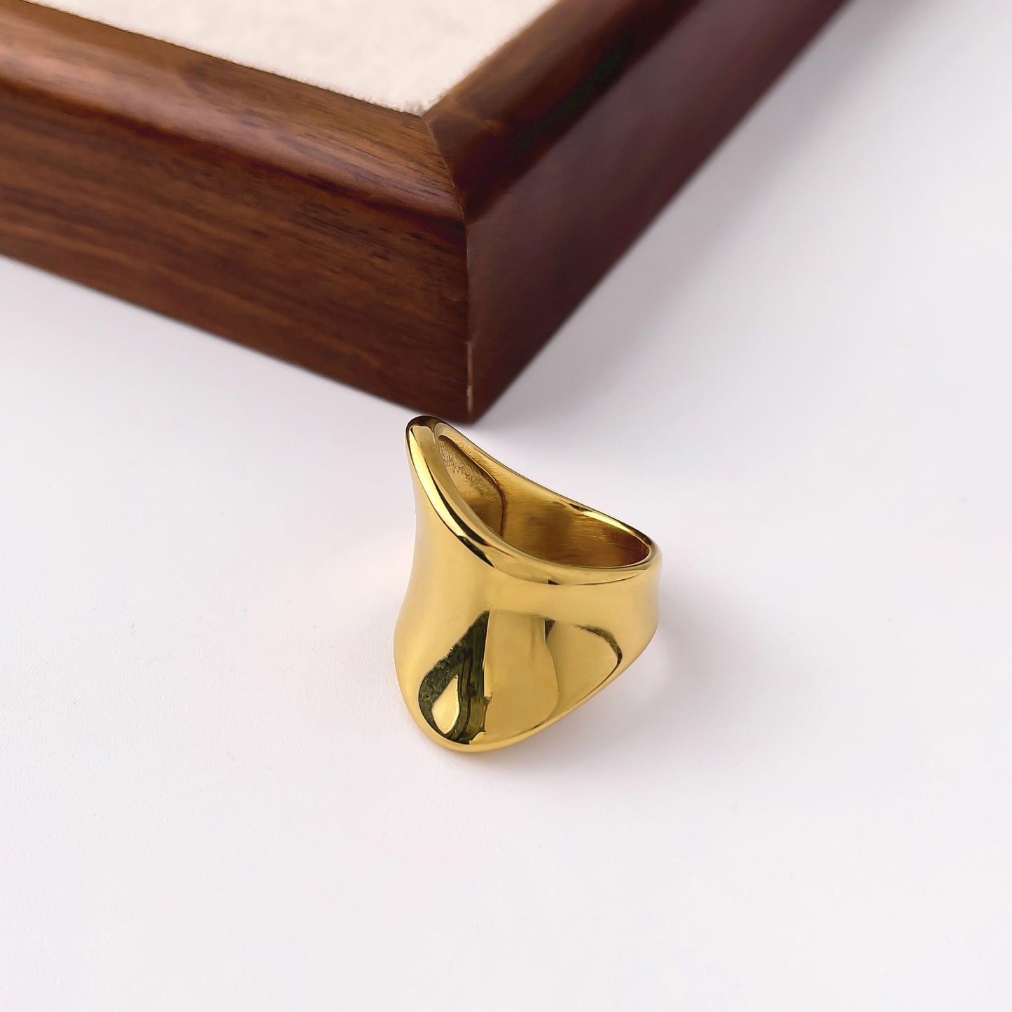 Skulptural ring i rostfritt stål guld minimalistisk design närbild liggandes mot vitbakgrund och trädetaljer
